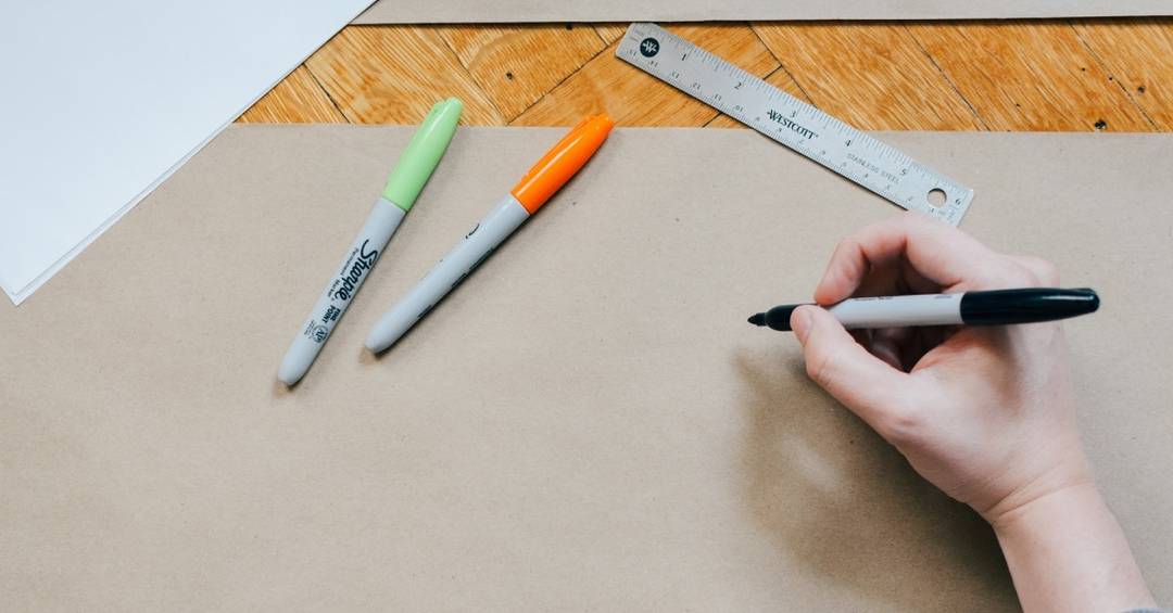 Ein Stift in einer Hand, der mit Filzstiften auf Zeichenkarton malt