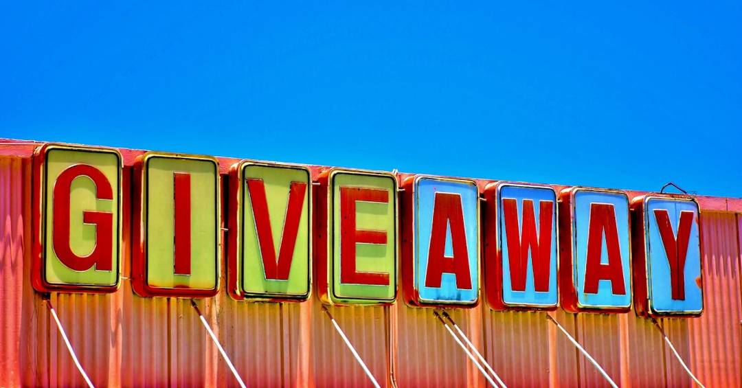 Der Schriftzug "Give Away" in rot, gelb und blau auf einem bunten Dach vor blauem Himmel