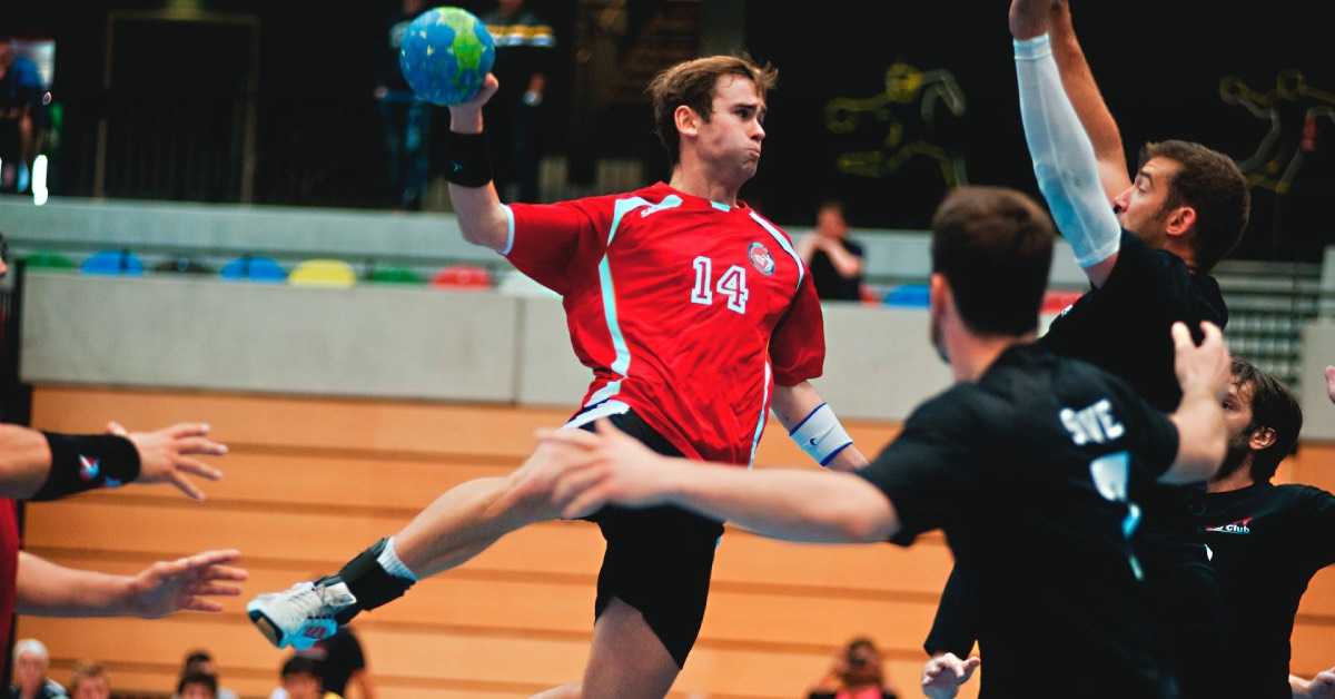 Ein Handballspieler mit Ball in der Hand springt inmitten eines Handballspiels nach oben und macht sich bereit, ins Tor zu werfen