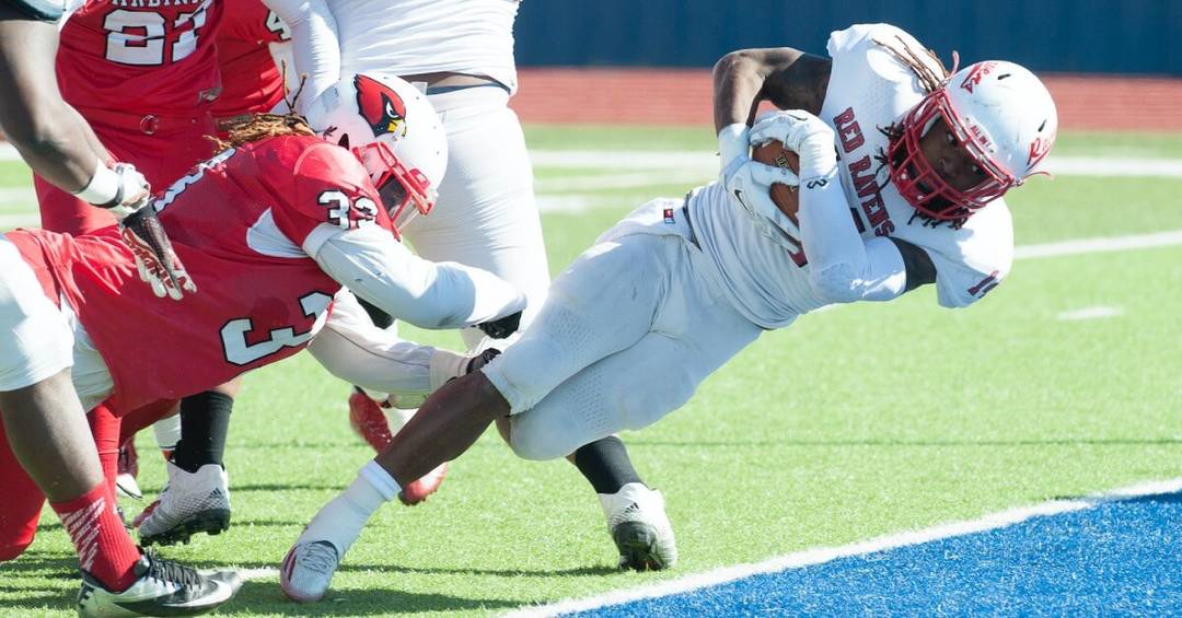 Vier American Football Spieler kämpfen um den Ball, ein Spieler im weißen Trikot hält den Ball fest umklammert