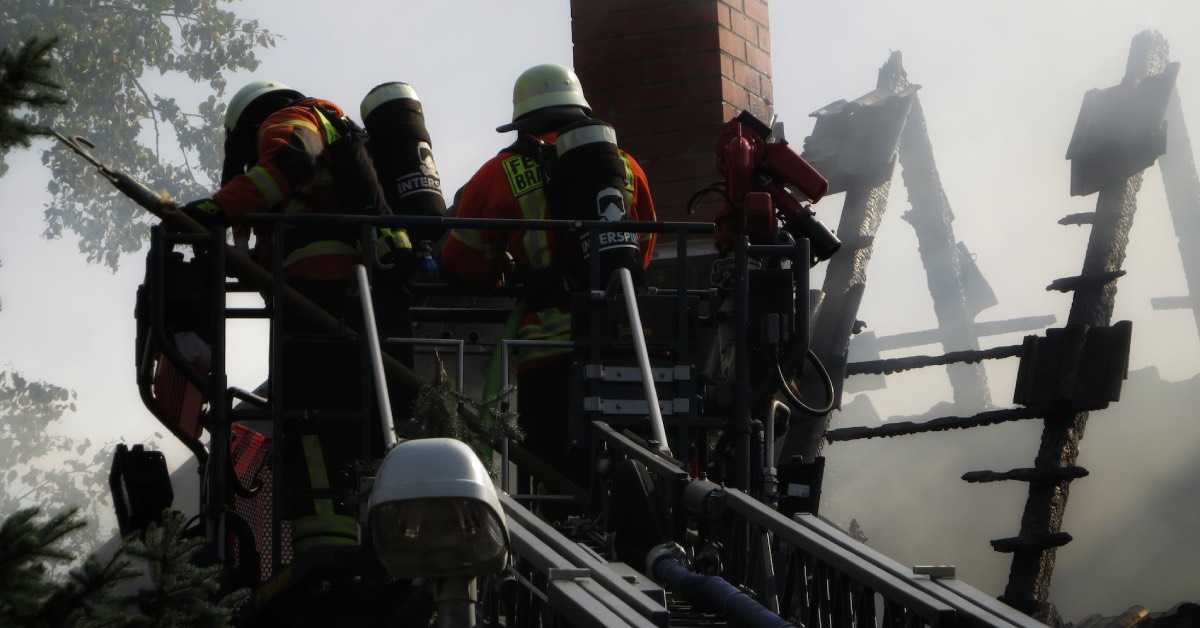 Feuerwehrleute auf einr Drehleiter begutachten einen ausgebrannten Dachstuhl