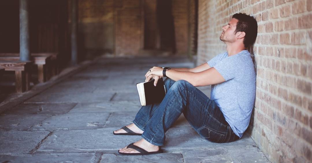 Ein junger Man sitzt verzweifelt an einer Mauer, in der Hand eine ausgedruckte Vereinssatzung