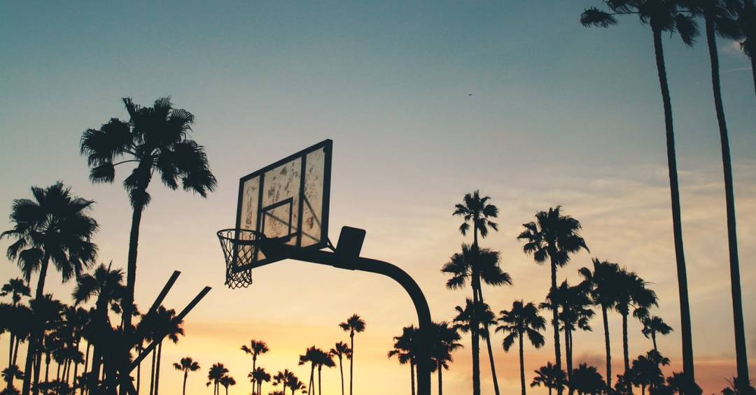 Ein Basketball Korb vor Palmen im Sonnenuntergang