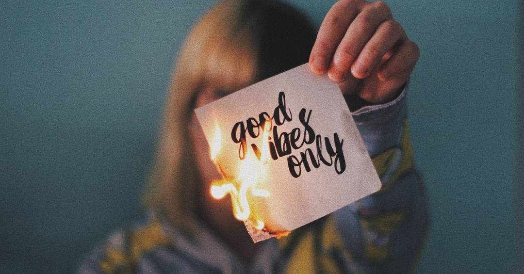Eine junge Frau hält einen brennenden Zettel in der Hand, mit der Aufschrift "Good Vibes Only"