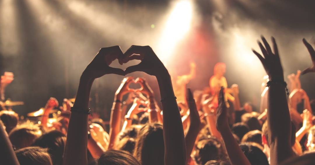 Eine Menschenmenge feiert auf einem Konzert, eine Besucherin hält die Hände nach oben und formt ein Herz