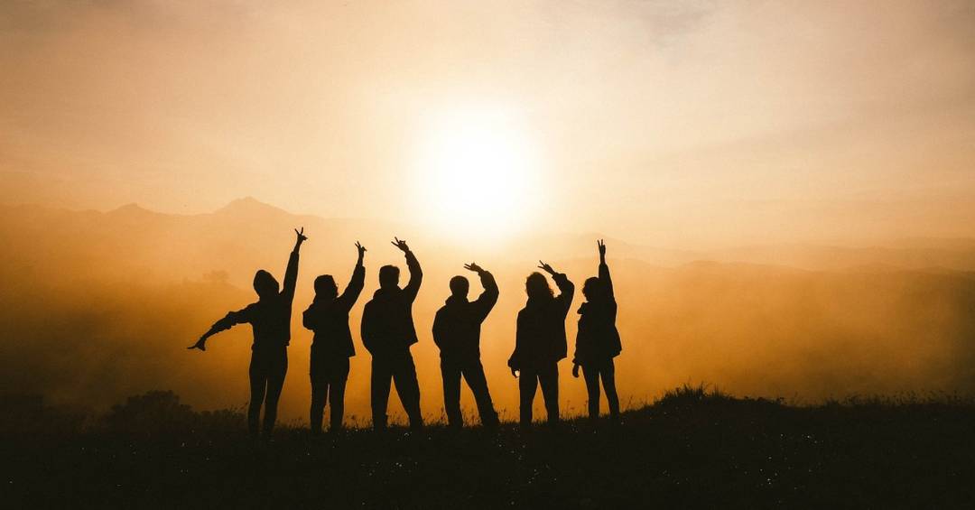 Eine Gruppe junger Menschen vor der untergehenden Abendsonne, es sind nur die Silhouetten zu sehen