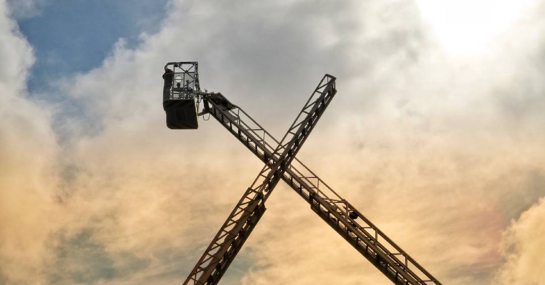 Zwei ausgefahrene Drehleitern berühren sich vor einem bewölkten Himmel